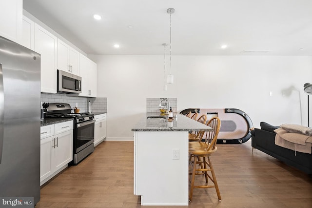 kitchen featuring backsplash, dark stone countertops, light wood-type flooring, appliances with stainless steel finishes, and white cabinets