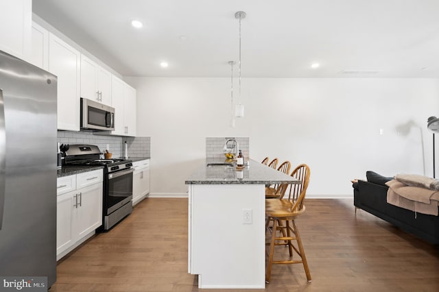 kitchen with light wood-type flooring, dark stone counters, tasteful backsplash, white cabinets, and stainless steel appliances