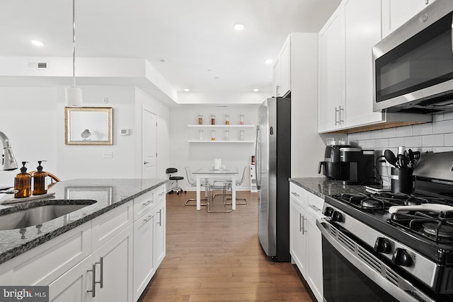 kitchen featuring dark stone counters, appliances with stainless steel finishes, wood-type flooring, decorative backsplash, and white cabinetry