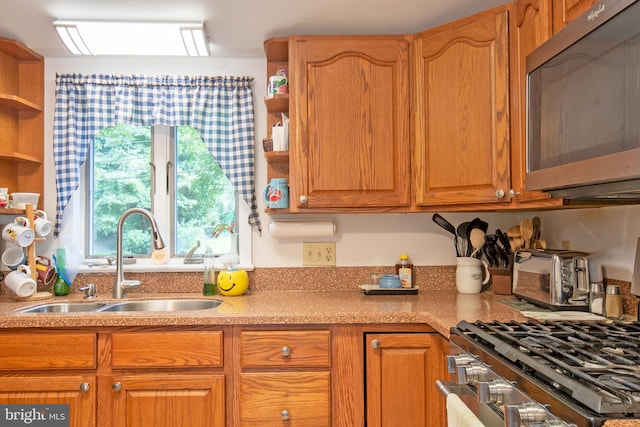 kitchen with brown cabinetry, appliances with stainless steel finishes, light countertops, open shelves, and a sink