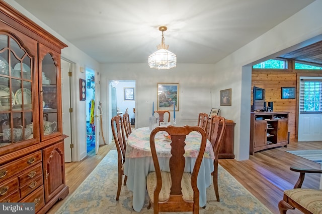 dining space featuring light hardwood / wood-style flooring, wooden walls, and an inviting chandelier