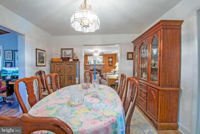 dining space featuring light wood finished floors, a fireplace, and ceiling fan with notable chandelier