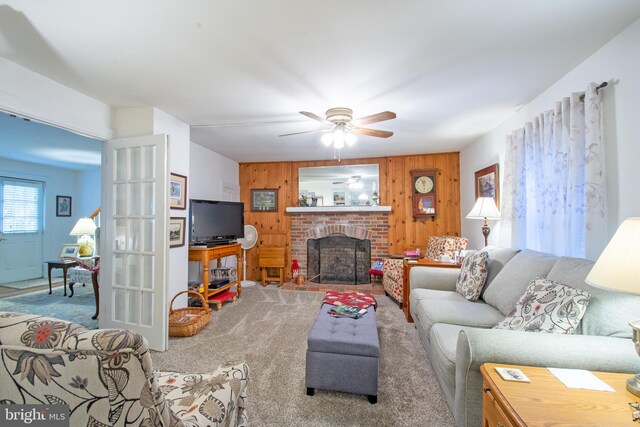 living room featuring wood walls, ceiling fan, a brick fireplace, and carpet flooring