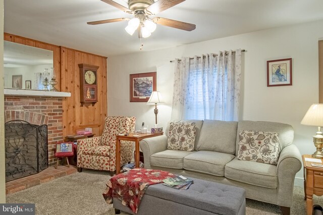 carpeted living room featuring ceiling fan, a fireplace, and wooden walls