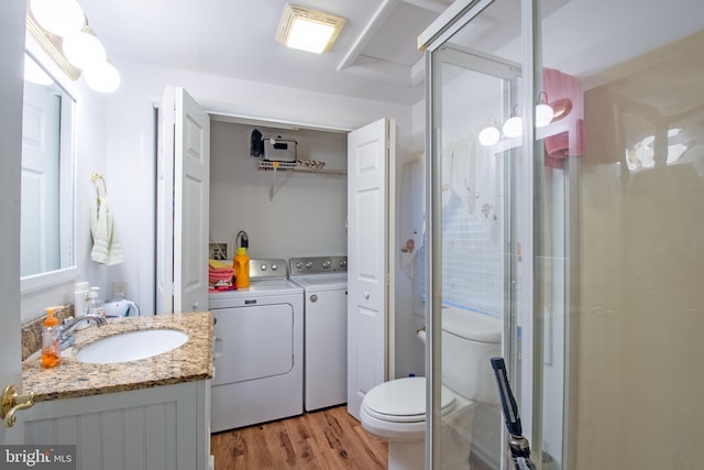 bathroom featuring wood-type flooring, a shower with shower door, washer and clothes dryer, vanity, and toilet