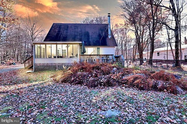 back of property at dusk with a sunroom, roof with shingles, and fence