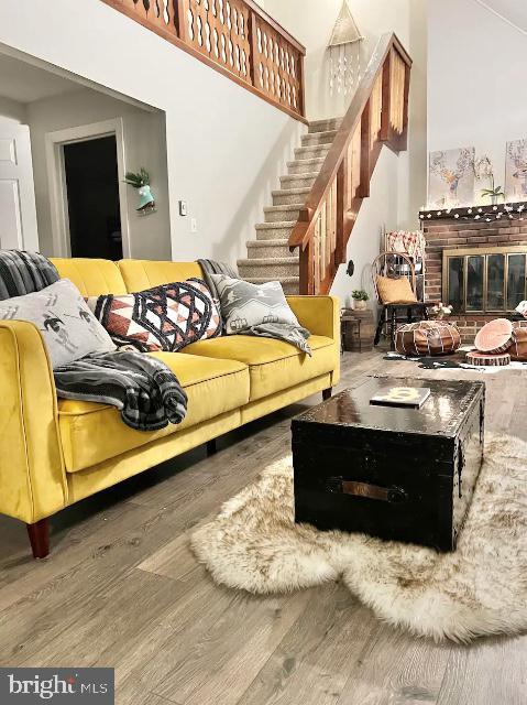 living room with a brick fireplace, stairs, and wood finished floors