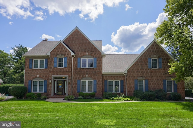 colonial home with a front yard, brick siding, and roof with shingles