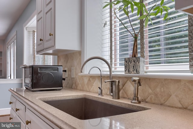 kitchen with white cabinetry, light stone counters, sink, and tasteful backsplash