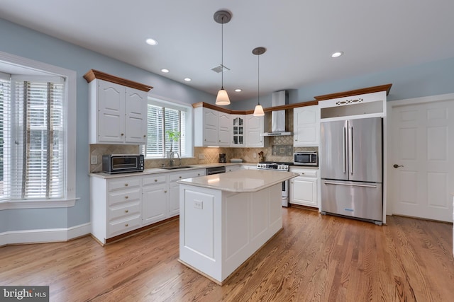 kitchen featuring decorative light fixtures, appliances with stainless steel finishes, light hardwood / wood-style floors, wall chimney range hood, and a kitchen island