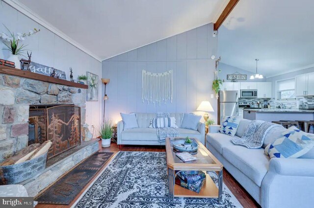 living room featuring wood-type flooring, crown molding, lofted ceiling with beams, and a stone fireplace