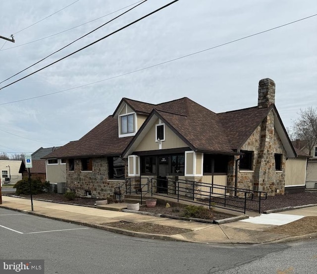 view of front of home with stone siding, central AC, and roof with shingles