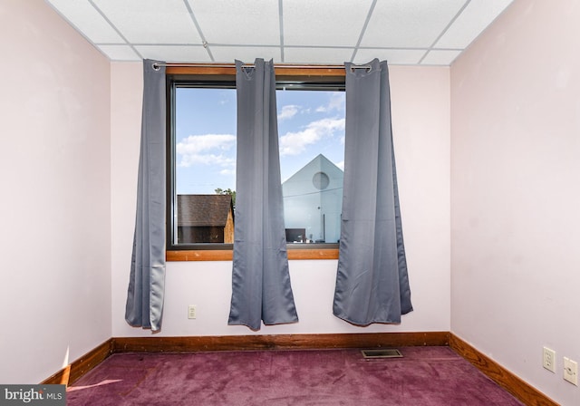 carpeted empty room featuring a drop ceiling and baseboards