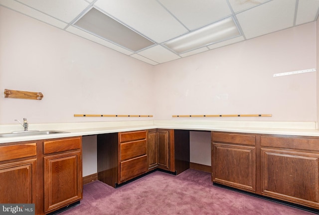 kitchen featuring built in study area, a drop ceiling, a sink, and carpet flooring