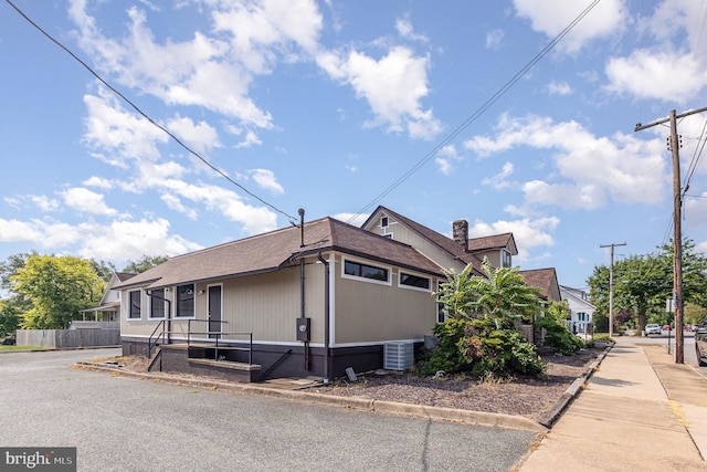 view of property exterior with roof with shingles, fence, and central AC unit