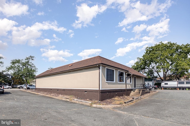 view of home's exterior with crawl space and roof with shingles