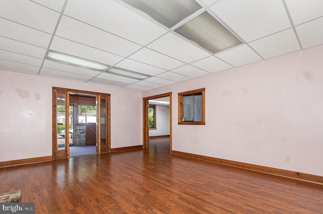 empty room featuring wood finished floors, a paneled ceiling, and baseboards