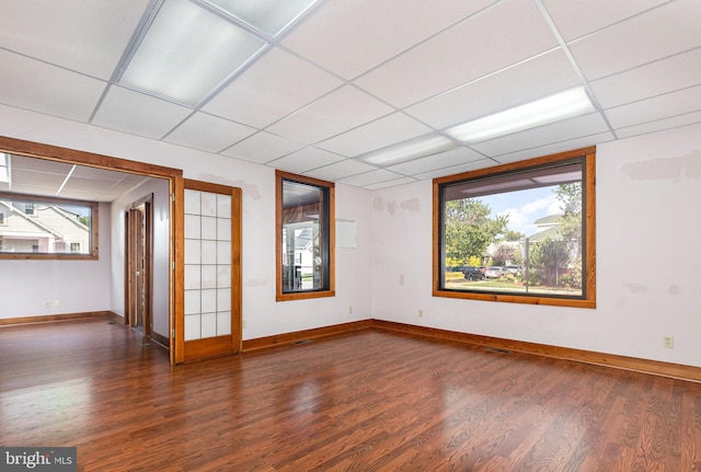 empty room featuring wood finished floors, a paneled ceiling, and baseboards