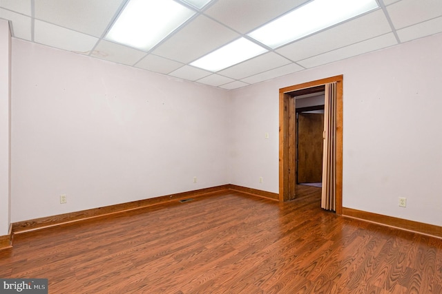 empty room with a drop ceiling, baseboards, and wood finished floors