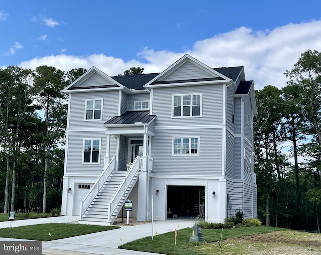 coastal home featuring a garage, concrete driveway, metal roof, a standing seam roof, and a front lawn