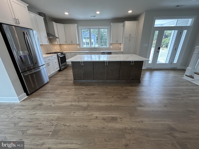 kitchen featuring wood-type flooring, white cabinetry, stainless steel appliances, a center island, and decorative backsplash