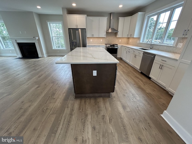 kitchen with white cabinets, wall chimney exhaust hood, a kitchen island, stainless steel appliances, and sink