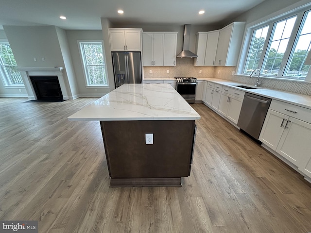 kitchen with white cabinets, sink, wall chimney range hood, appliances with stainless steel finishes, and a center island