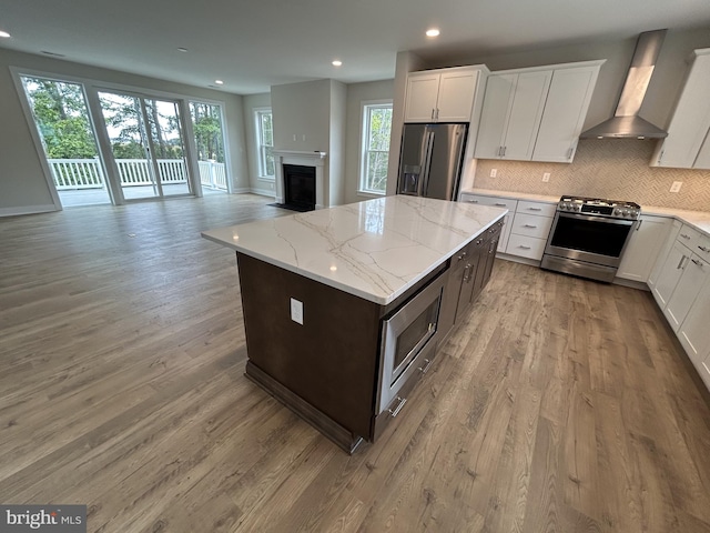 kitchen with white cabinets, stainless steel appliances, wall chimney range hood, and a healthy amount of sunlight