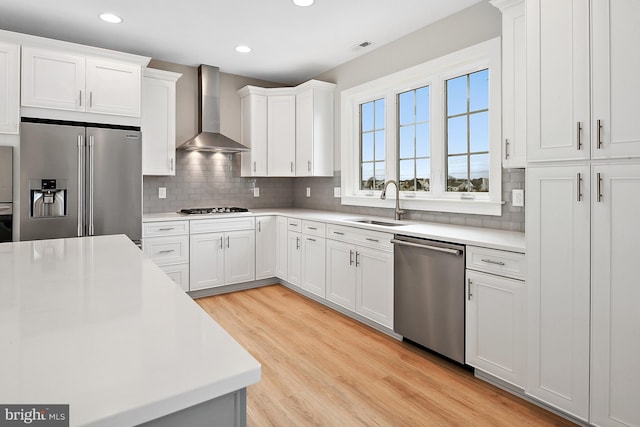 kitchen featuring white cabinets, sink, wall chimney exhaust hood, light hardwood / wood-style flooring, and appliances with stainless steel finishes