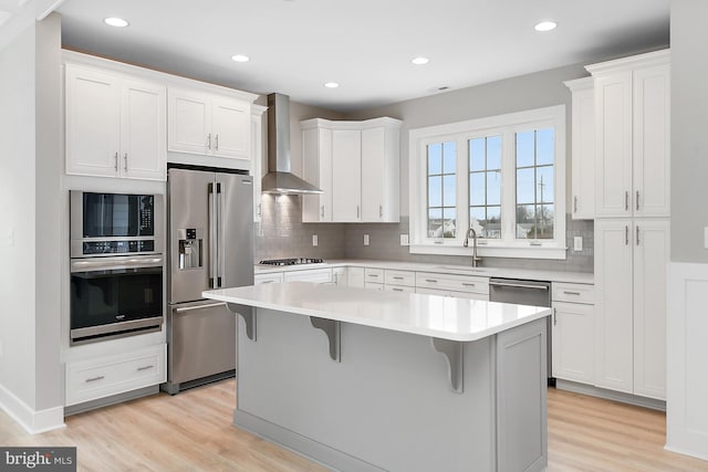 kitchen featuring wall chimney exhaust hood, stainless steel appliances, white cabinets, and a center island