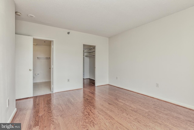 unfurnished bedroom featuring a textured ceiling, hardwood / wood-style floors, a walk in closet, and a closet