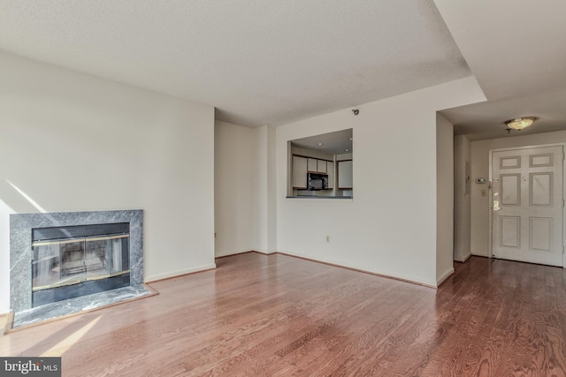 unfurnished living room with hardwood / wood-style flooring, a textured ceiling, and a high end fireplace