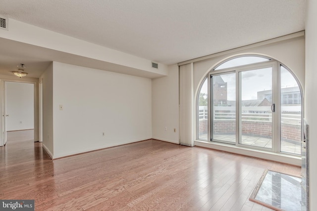 unfurnished room with wood-type flooring, a textured ceiling, and a healthy amount of sunlight