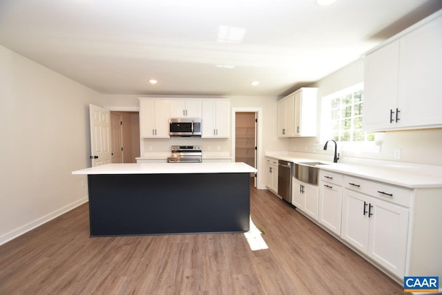 kitchen with white cabinets, a center island, stainless steel appliances, light countertops, and a sink