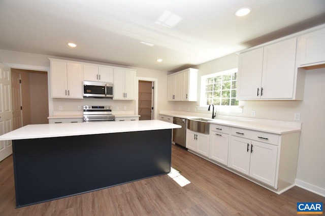 kitchen with light countertops, appliances with stainless steel finishes, white cabinetry, a kitchen island, and wood finished floors