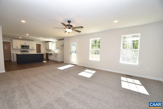 unfurnished living room featuring ceiling fan, recessed lighting, a sink, baseboards, and dark colored carpet