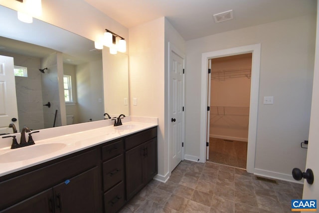 bathroom featuring double vanity, visible vents, a sink, and tiled shower