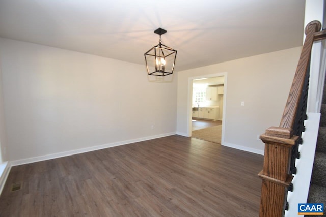 spare room with dark wood-style flooring, a notable chandelier, baseboards, and stairs