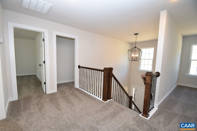 corridor featuring baseboards, visible vents, carpet flooring, an upstairs landing, and a notable chandelier