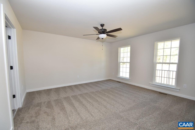 empty room featuring a ceiling fan, light colored carpet, visible vents, and baseboards