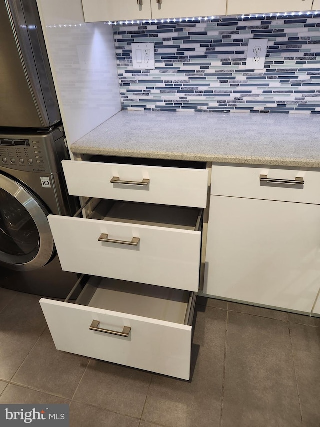 washroom with stacked washer and clothes dryer and dark tile patterned flooring