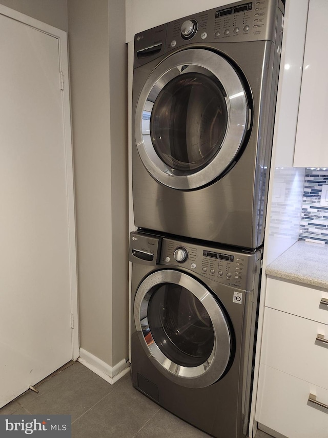 laundry area featuring stacked washer and clothes dryer, dark tile patterned flooring, and cabinets