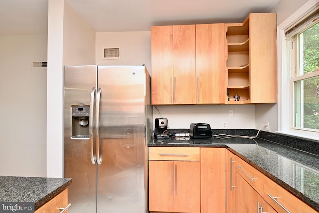 kitchen with a wealth of natural light, stainless steel fridge, and dark stone countertops