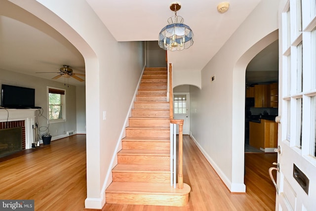 stairway with a fireplace, ceiling fan with notable chandelier, and wood-type flooring