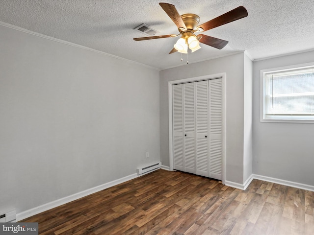 unfurnished bedroom with a baseboard radiator, visible vents, a closet, dark wood finished floors, and crown molding