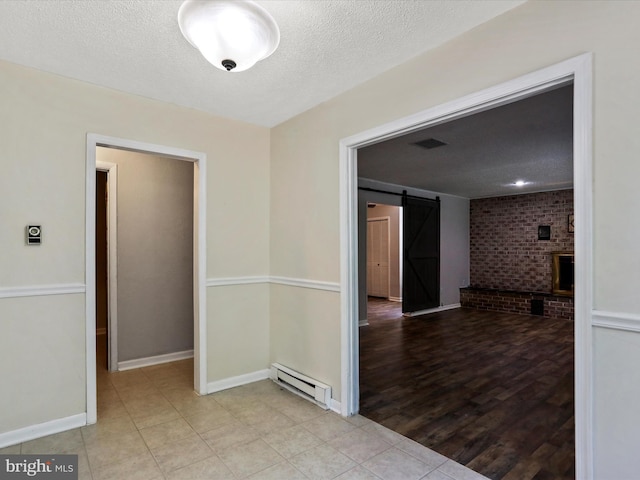 unfurnished room featuring a textured ceiling, a barn door, visible vents, baseboards, and baseboard heating