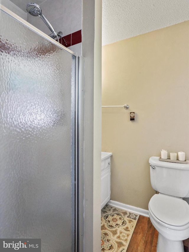 full bathroom with a textured ceiling, toilet, wood finished floors, baseboards, and a shower stall