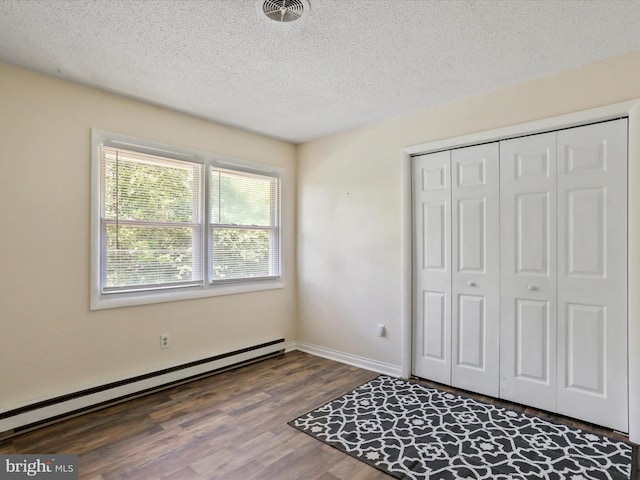 unfurnished bedroom featuring visible vents, wood finished floors, baseboard heating, a textured ceiling, and a closet