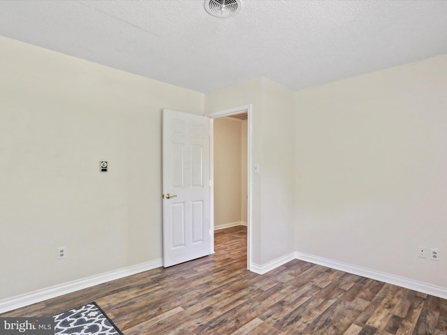 unfurnished room featuring baseboards, a textured ceiling, visible vents, and dark wood-style flooring