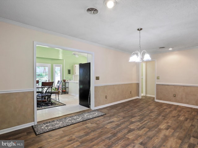 unfurnished dining area with a wainscoted wall, crown molding, visible vents, an inviting chandelier, and wood finished floors